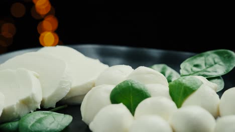 pequeñas bolas de queso mozzarella blancas, hojas de espinaca en un plato negro.