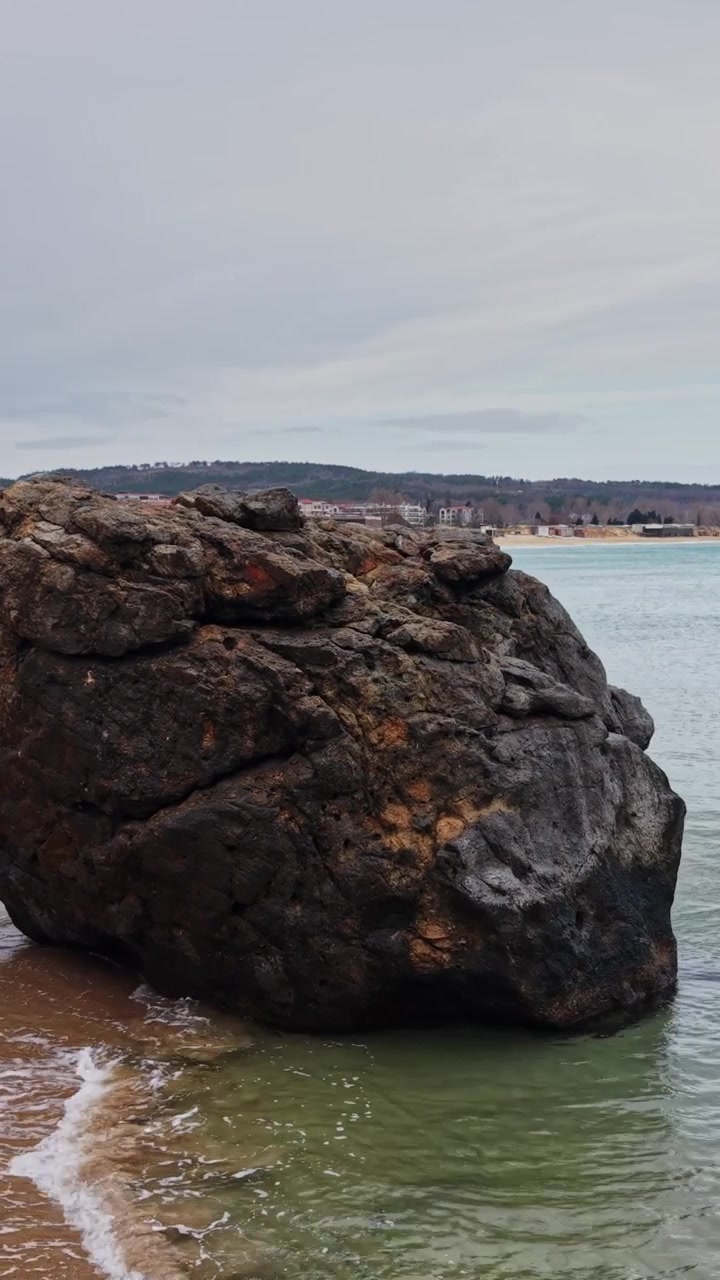 Klippe står på sandstrand nær det rolige hav på en overskyet dag