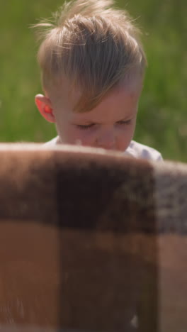 a young boy in a white shirt holds onto the edge of a flowing plaid scarf in a grassy field as the wind gently blows. on a sunny day