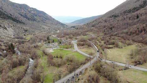 aerial: passenger train in a valley crossing a river on ancient viaduct in the pyrenees, southern france