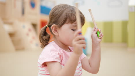 Happy-Face-of-3-year-old-Girl-While-Playing-on-Xylophone-striking-with-Millets-on-Keyboards-in-Turn-at-Indoor-Playroom---Portrait-Close-up