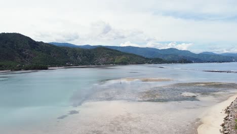 Aerial-drone-rising-above-a-solo-fishermen-at-low-tide-on-coral-reefs-on-tropical-island-Timor-Leste,-South-East-Asia