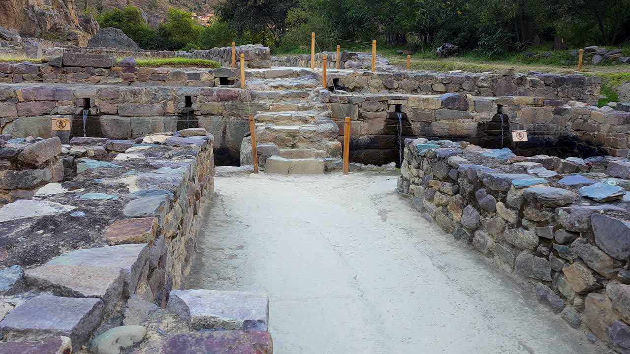 A serene pathway leads through ancient Inca stone structures toward the ceremonial Inka Misana. This historic site in Ollantaytambo Archaeological Park showcases impressive stonework