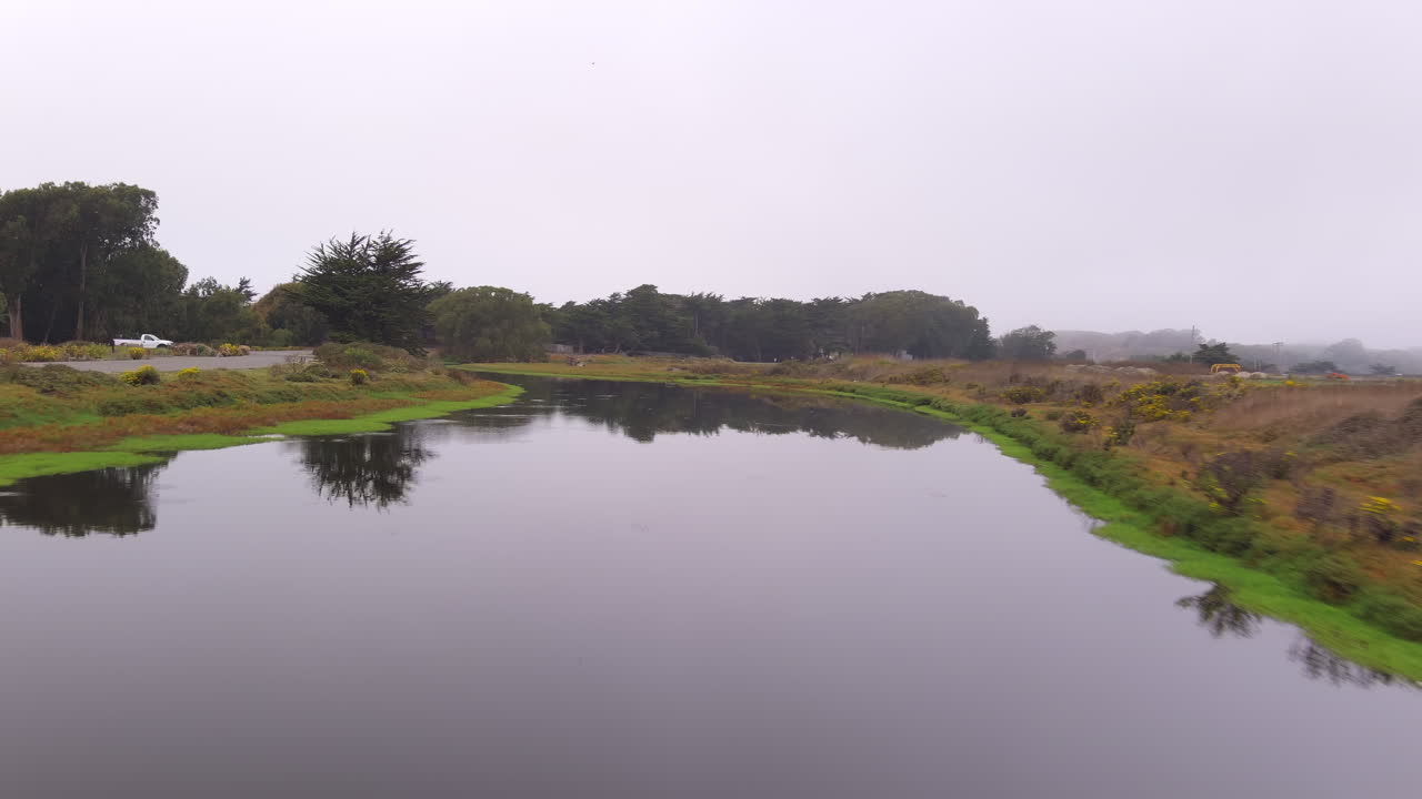 vista panorámica aérea desde arriba de un canal de agua con árboles, caminos, casas y postes de luz junto a sus orillas al atardecer