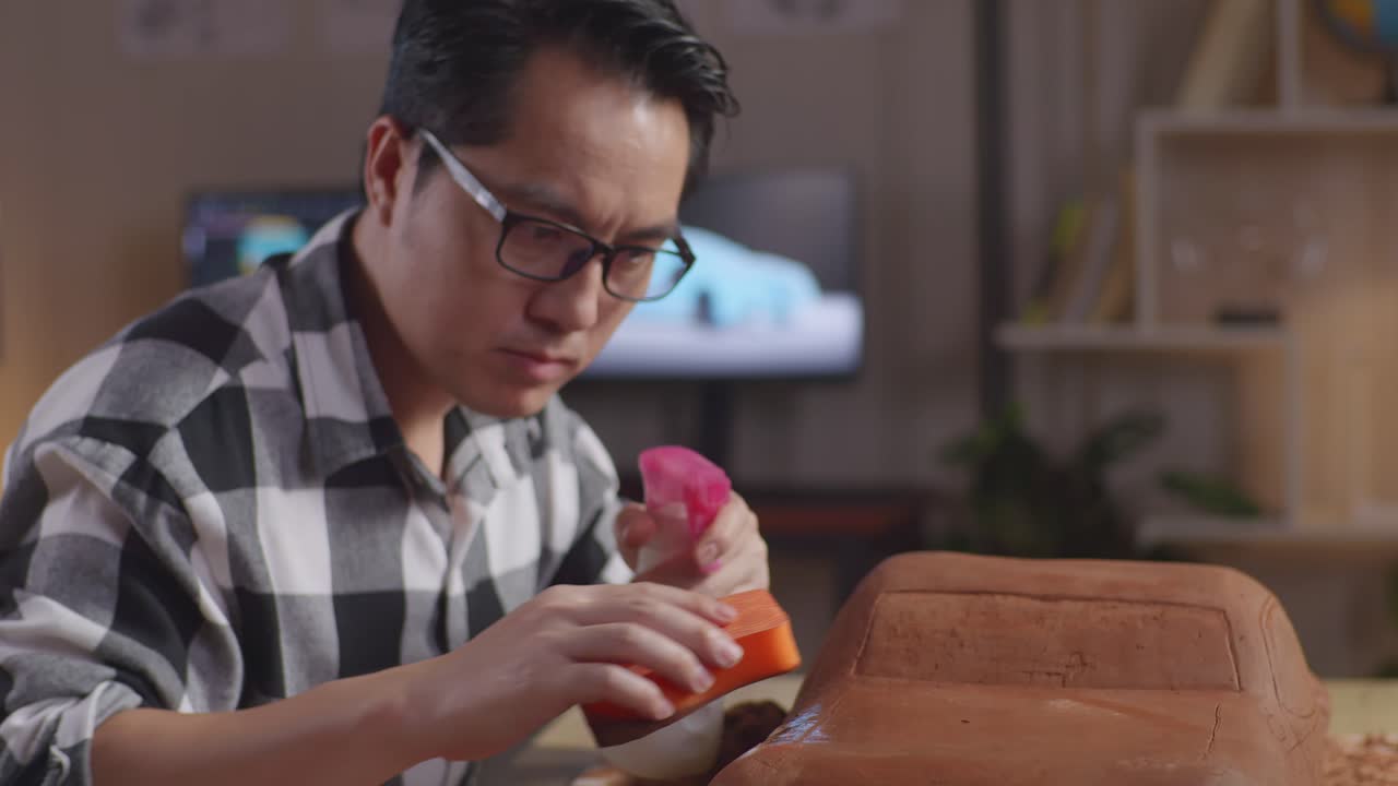 primer plano de un hombre asiático diseñador de automóviles rociando y usando esponja para suavizar la superficie de la escultura de arcilla de coche en el estudio