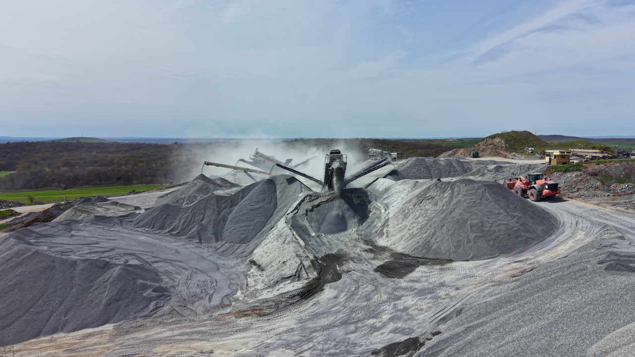 Operasi penambangan granit dengan alat berat di area terbuka pada hari yang cerah.