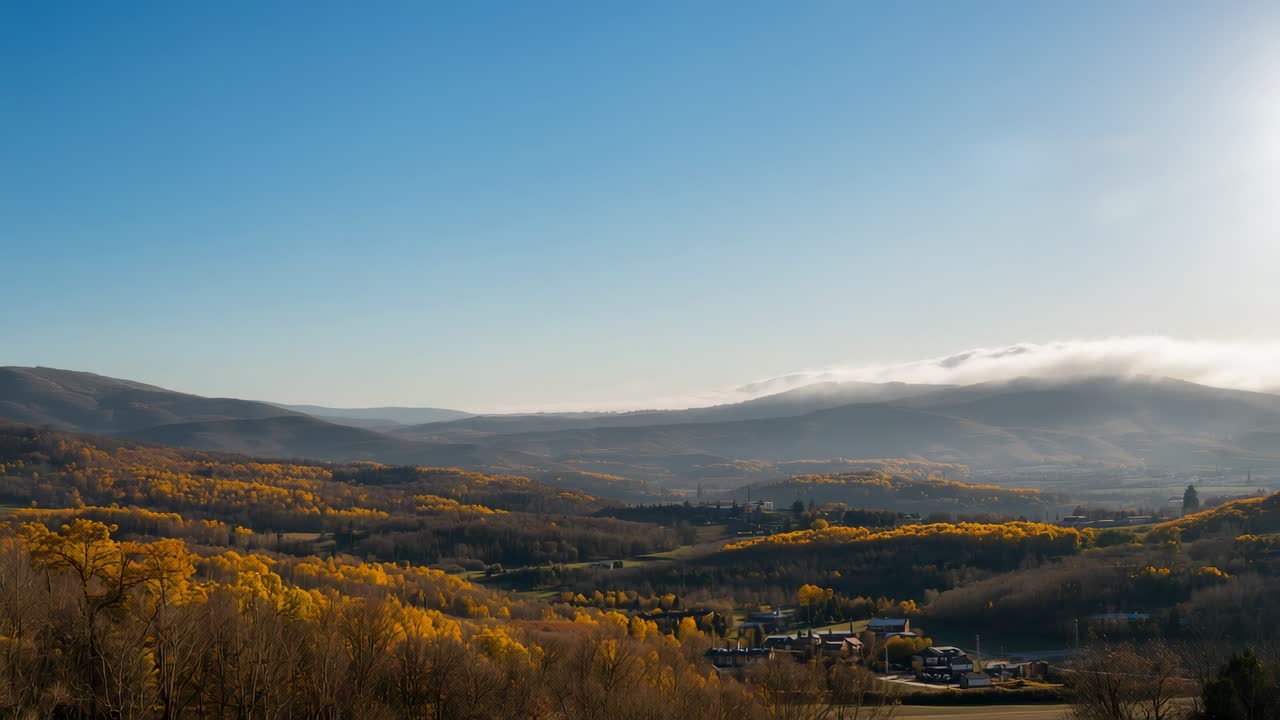 Low fog bank drifting across valley at dawn after sunrise, with farmhouses, autumn foliage
