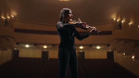 portrait of young woman with violin in hands on scene of opera house or philharmonic hall