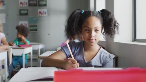 Video-Eines-Fokussierten-Gemischtrassigen-Mädchens,-Das-Im-Klassenzimmer-Am-Schreibtisch-Sitzt