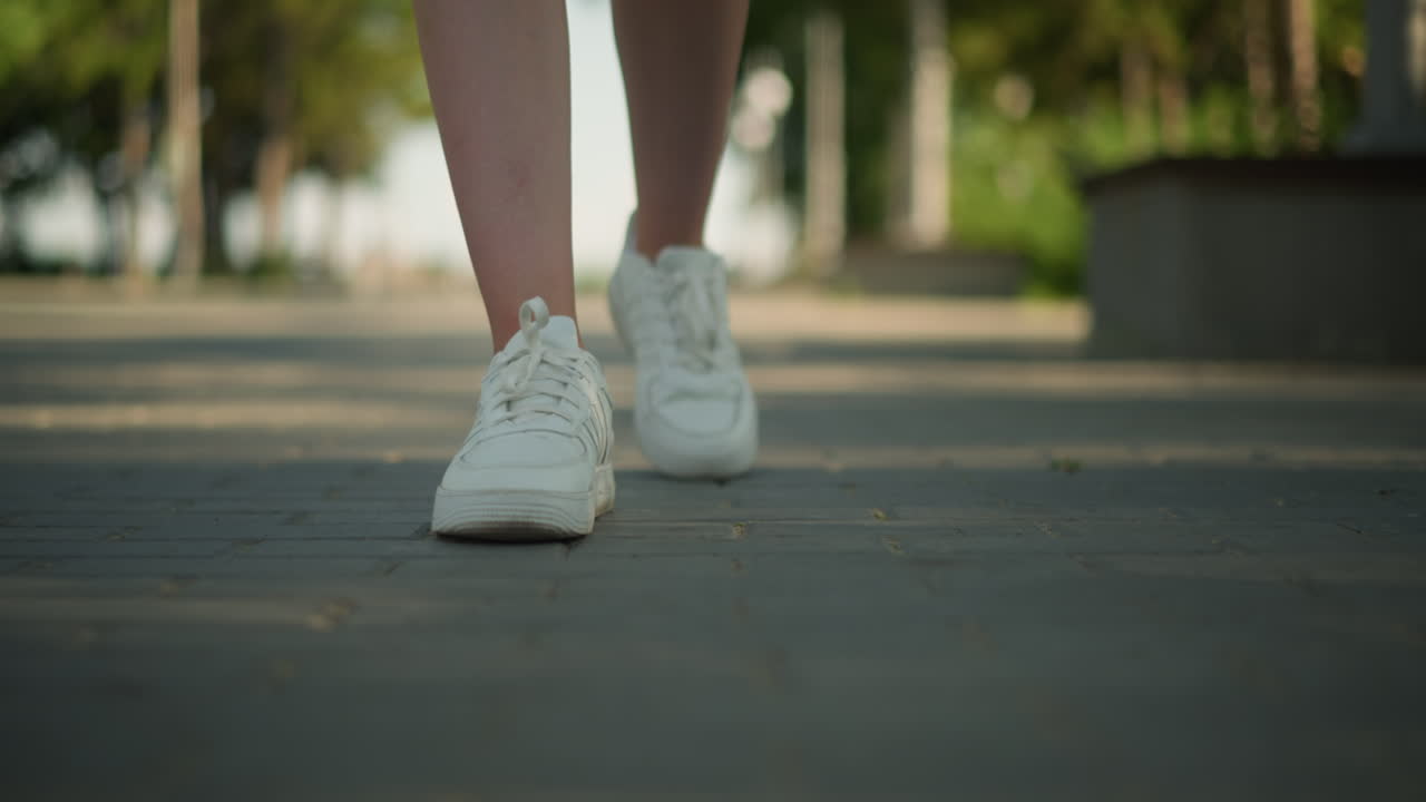 vista de cerca de la pierna de un individuo con zapatillas blancas caminando por un camino entrelazado bajo la cálida luz del sol, con un fondo borroso con árboles altos, vegetación exuberante y un entorno al aire libre sereno