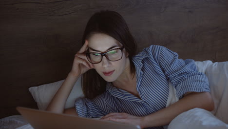 그녀의 침대에서 저녁에 뭔가를 보면서 노트북을 사용하고 웃는 여자의 근접 촬영보기