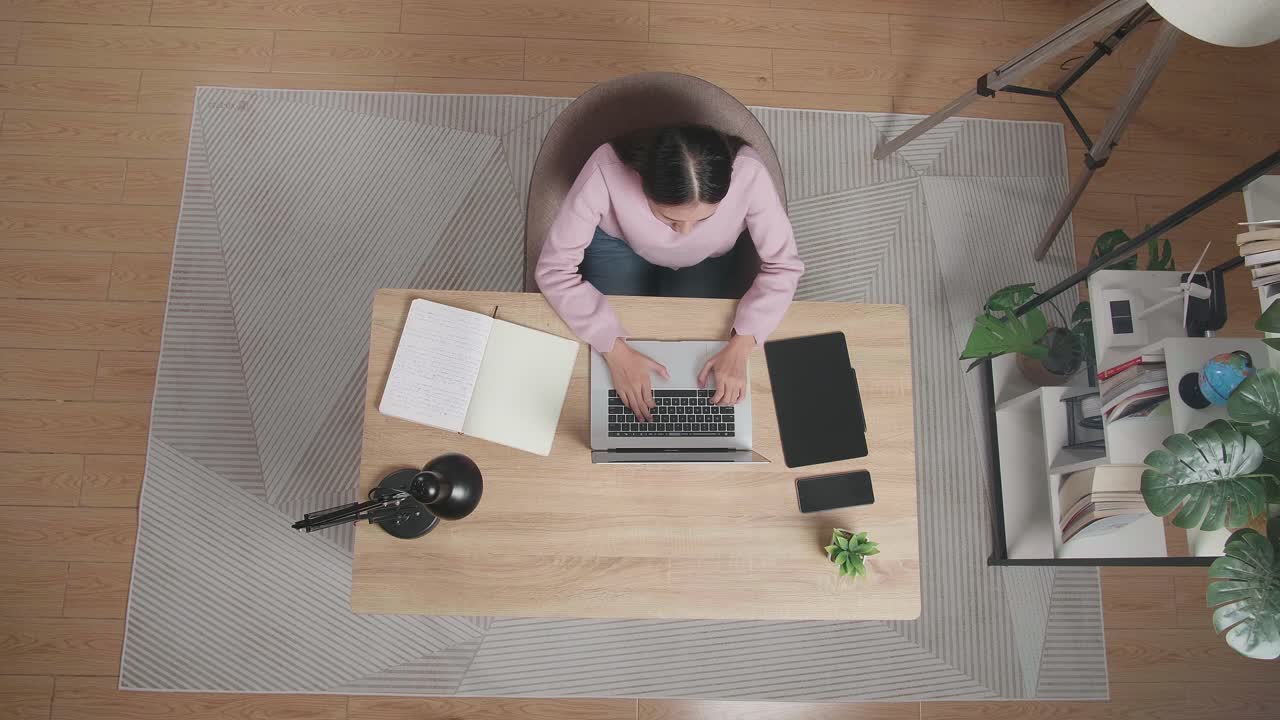 Top View Of A Woman Typing On A Laptop While Sitting At The Wooden Desk At Home