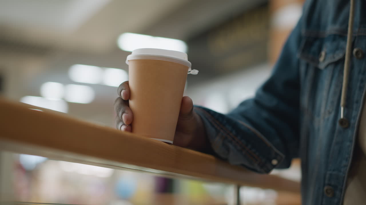 Close-up of hand holding paper coffee cup, resting on wooden railing in modern indoor setting, with soft focus background, symbolising peaceful moment of calm and relaxation