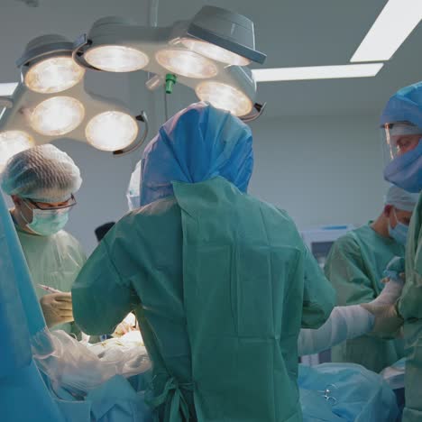 surgery at pandemic time. group of medical specialists in protective uniform doing an operation to a patient under medical lamp in clinic
