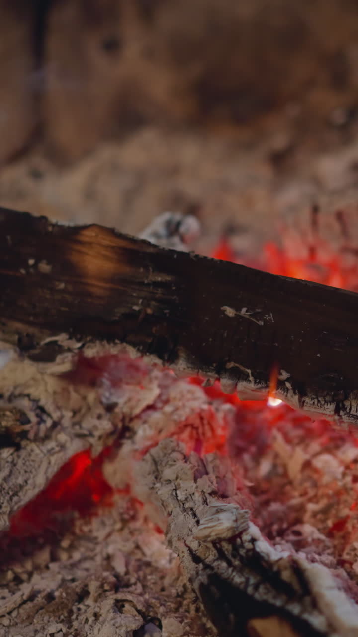Wood piece burns in hot ash pile at fireplace macro view. Campfire with sticks and hot charcoal. Way to get calm and warm atmosphere