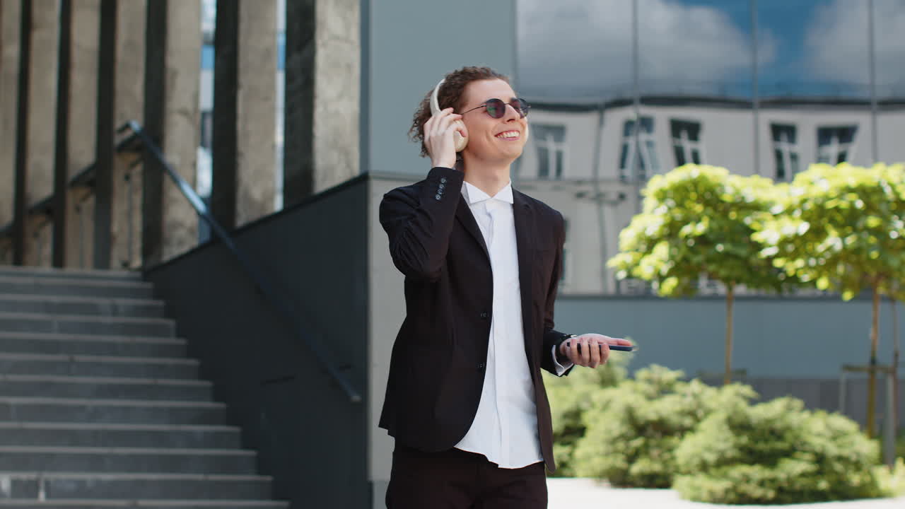 Happy relaxed young caucasian businessman in wireless headphones dancing listening music outdoors