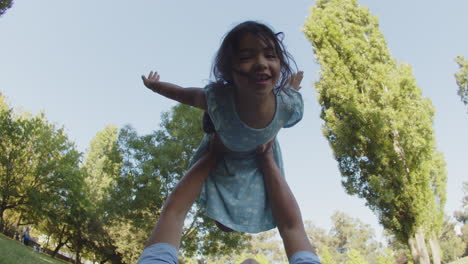 father lying on ground and raising his smiling daughter on hands