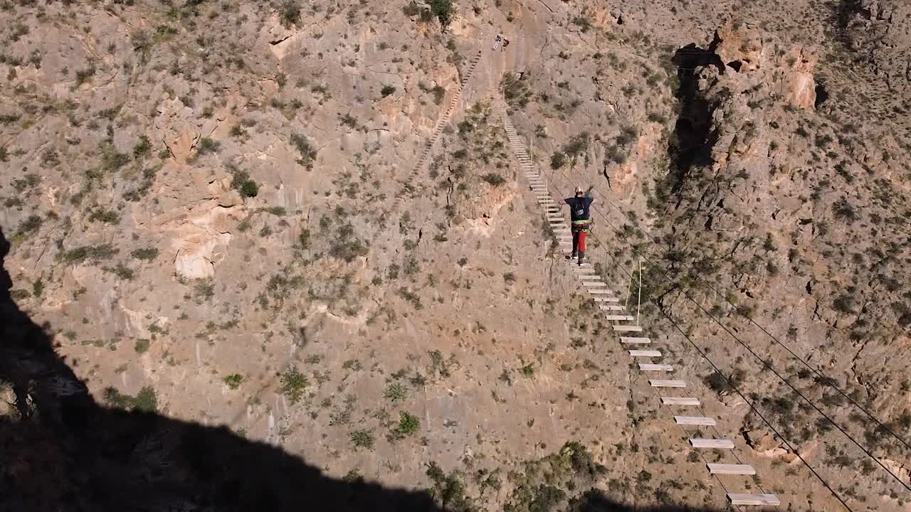Sportman crossing suspended bridge between mountains in via ferrata