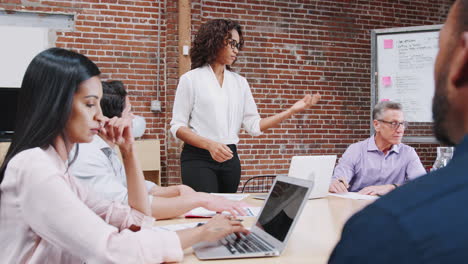 Empresaria-De-Pie-Y-Líder-De-La-Reunión-De-Oficina-Alrededor-De-La-Mesa