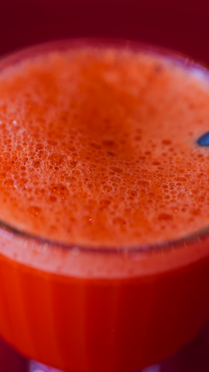 Primo piano di un succo di carota e arancia in un bicchiere con una cannuccia nera su una tovaglia rossa. Verticale