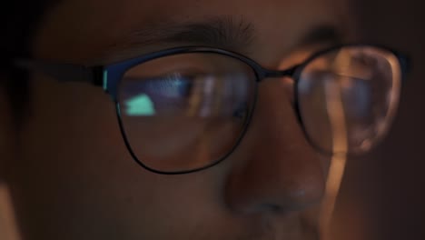 man traiding at night looking at monitor, reflections in eyeglasses