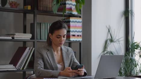 stylish young woman uses a smartphone surf the internet sitting at a table in modern cafe smiling. young business woman indoors in office using mobile phone
