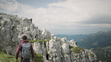 young hiker climbing up a mountainon green path among the rocks, valley visible in background