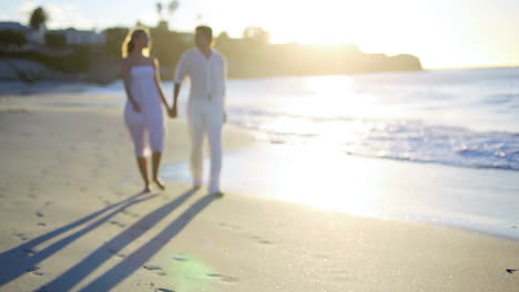 couple holding hands as they walk away from the sunset on the beach