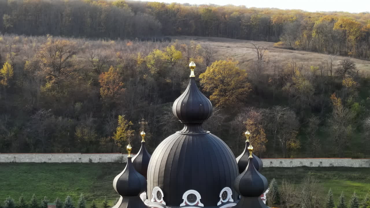 Experience the stunning view of a historic church with a golden dome set against a backdrop of colorful autumn trees and hills. Nature combines with rich architecture