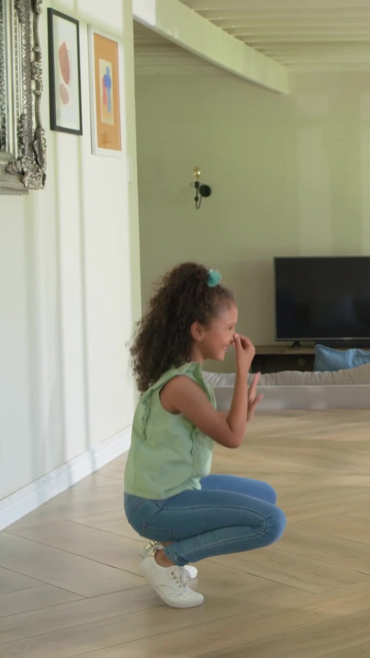 Vertical video: Dancing girl after small bounce, practicing routine at home on floor, in green top