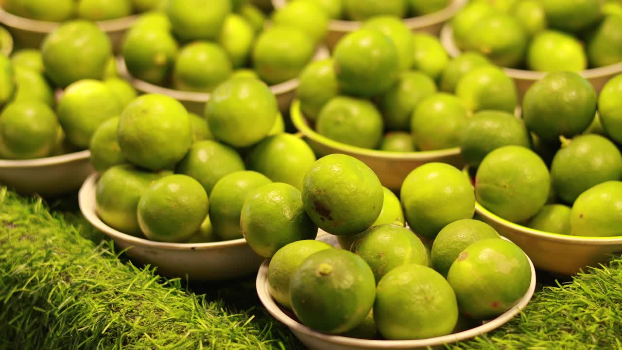 Bright green limes arranged in bowls on artificial turf, captured at a floating market with warm lighting