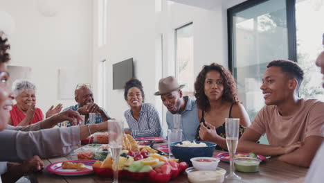 tres generaciones de una familia negra sentada en la mesa de cenar celebrando juntos, de cerca