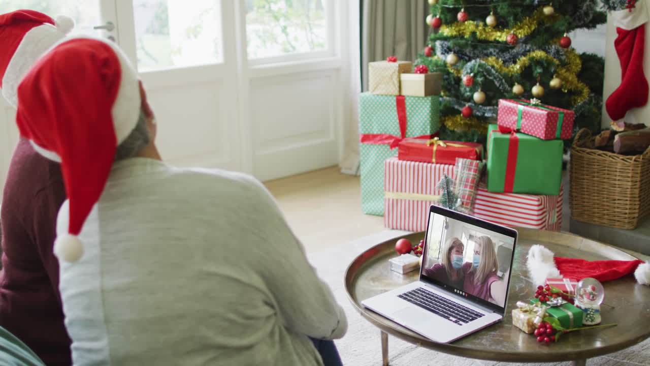 diversas amigas mayores que usan una computadora portátil para una videollamada de navidad con una familia feliz en la pantalla