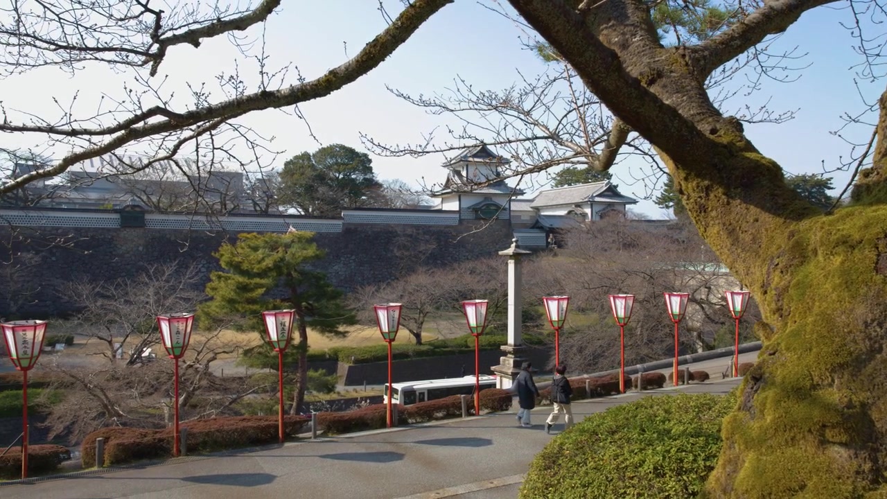Toma estática de arquitectura de castillo antiguo y farolillos rojos a través de árboles cubiertos de musgo en Kanazawa, Japón