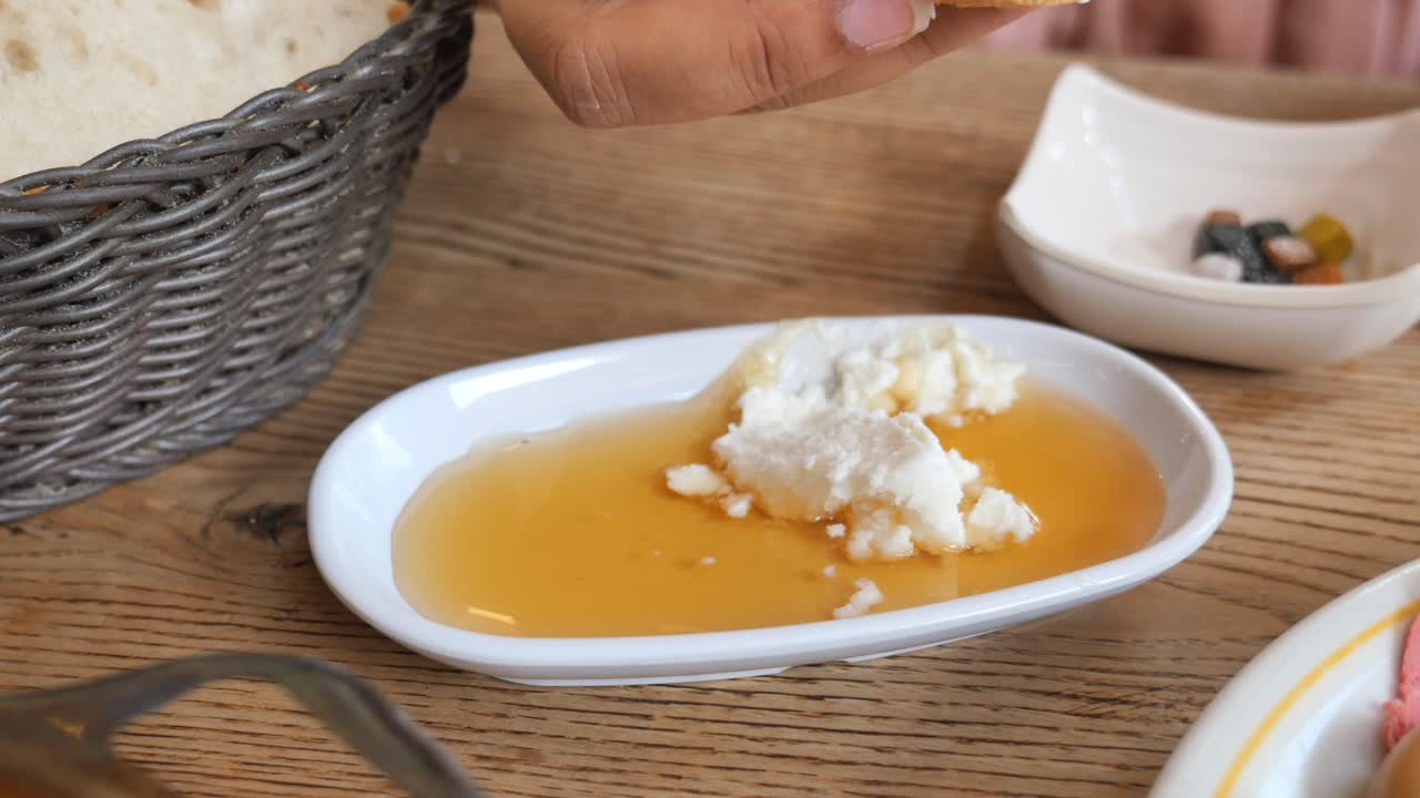 человек, погружающий хлеб в тарелку с медом и сыром
