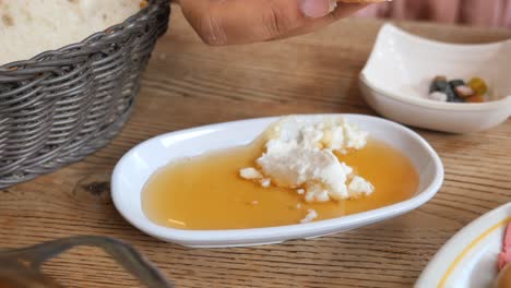 a person dipping bread into a plate of honey and cheese