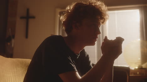 depressed young man praying and emotionally crying in sunlit room