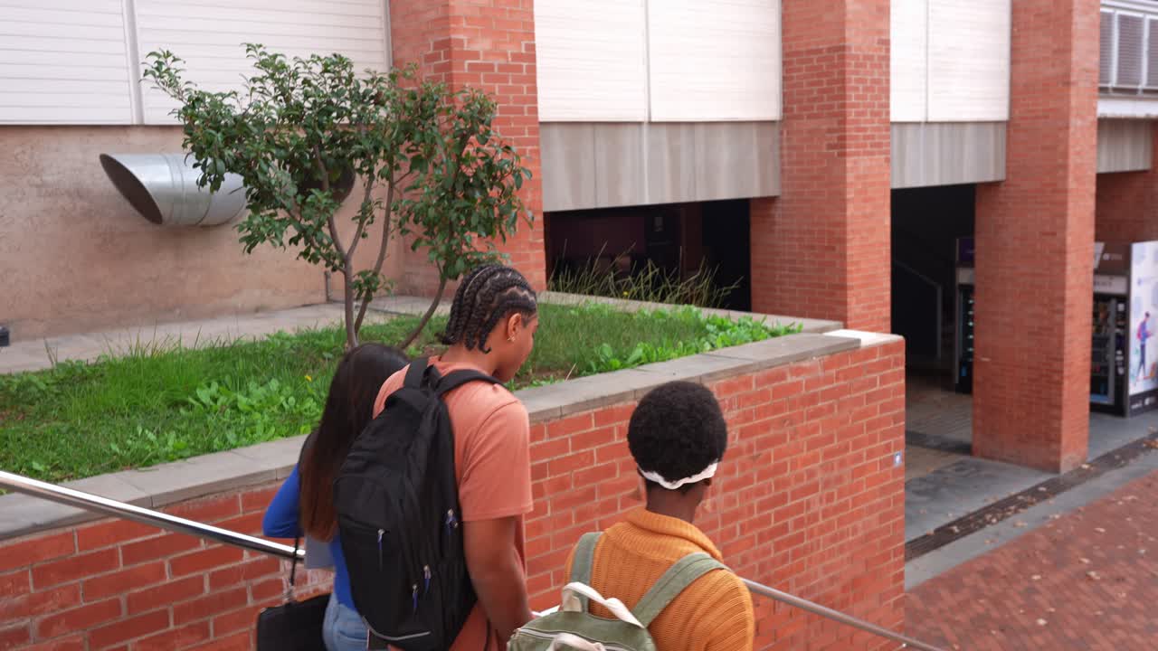 Estudiantes diversos con mochilas bajando escaleras en un campus universitario