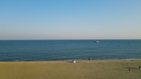 Gente-Caminando-Tranquilamente-En-El-Parque-Junto-Al-Mar-Con-Un-Barco-De-Pesca-Navegando-En-El-Océano-Azul