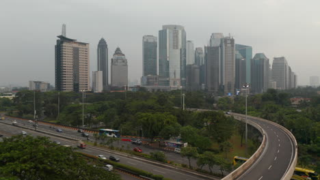 Ascending-aerial-pedestal-shot-passing-the-overpass-with-busy-car-traffic-and-revealing-Jakarta-city-cityscape-with-skyscrapers