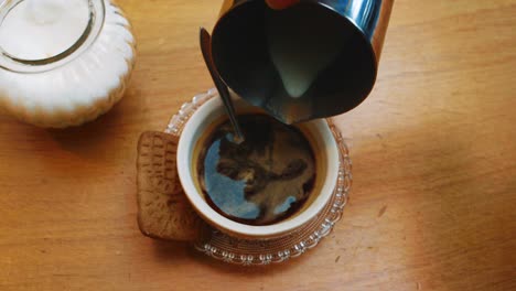 adding cream or milk to coffee with biscuit on wooden table, top down view