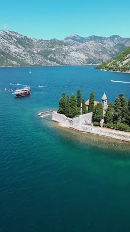 vertical aerial view of montenegro landscape with small island in the middle of kotor bay. drone circling arround the islands. famous travel destination. tourist boats passing. turquoise water color.
