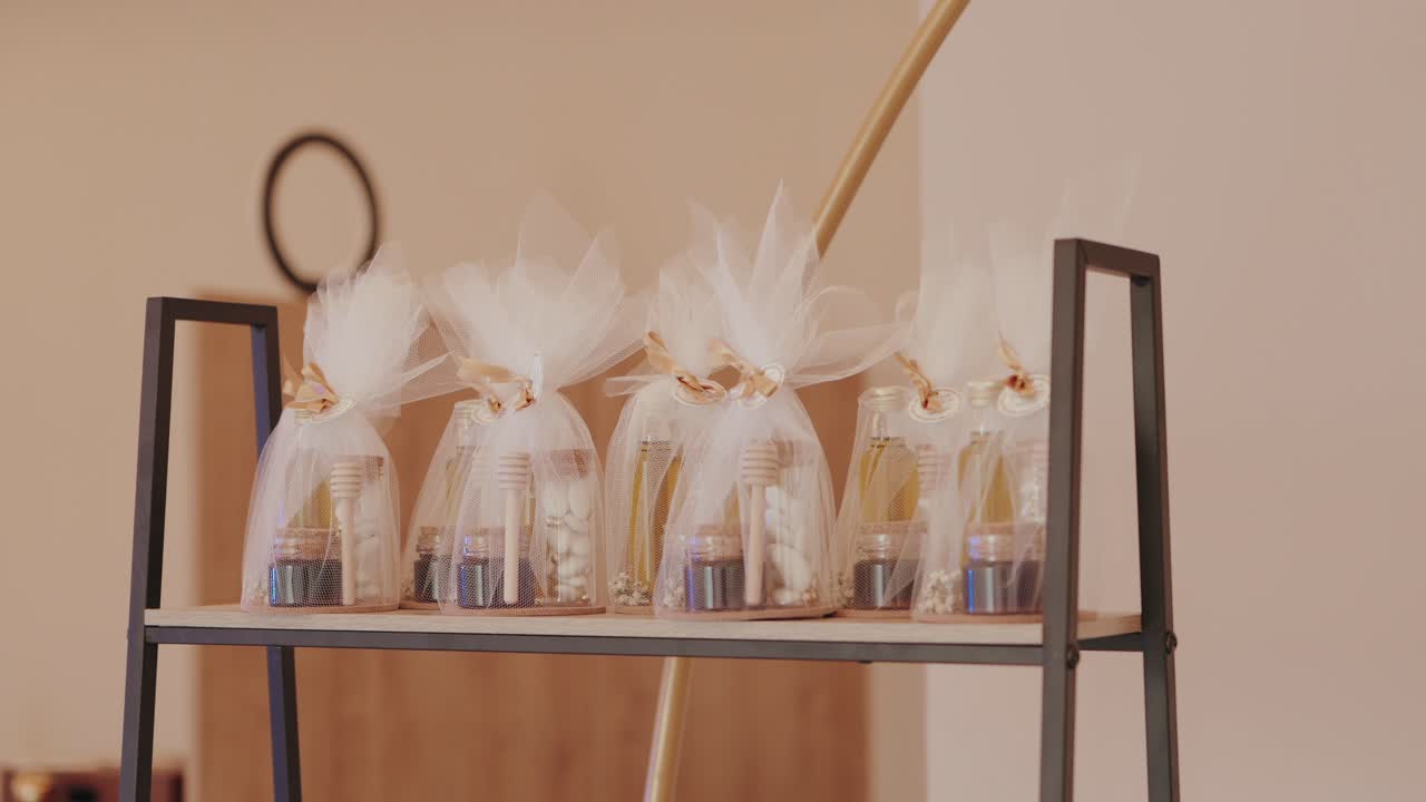 진열대 선반 위에 꿀단지가 있는 결혼식 답례품과 흰색 튤로 포장된 선물이 놓여 있어요.