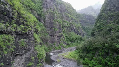 drone footage of a river in a deep jungle canyon in the cirque of mafate on the reunion island with a small green tent in the middle