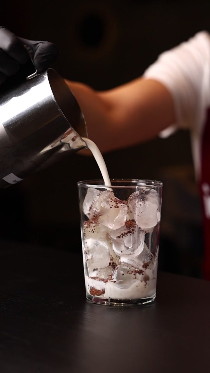 Barista che versa il latte in un bicchiere con cubetti di ghiaccio