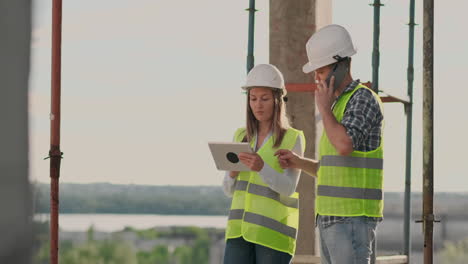 Building-in-construction-with-a-female-and-a-male-builders-constructors-engineers-walking-along-it