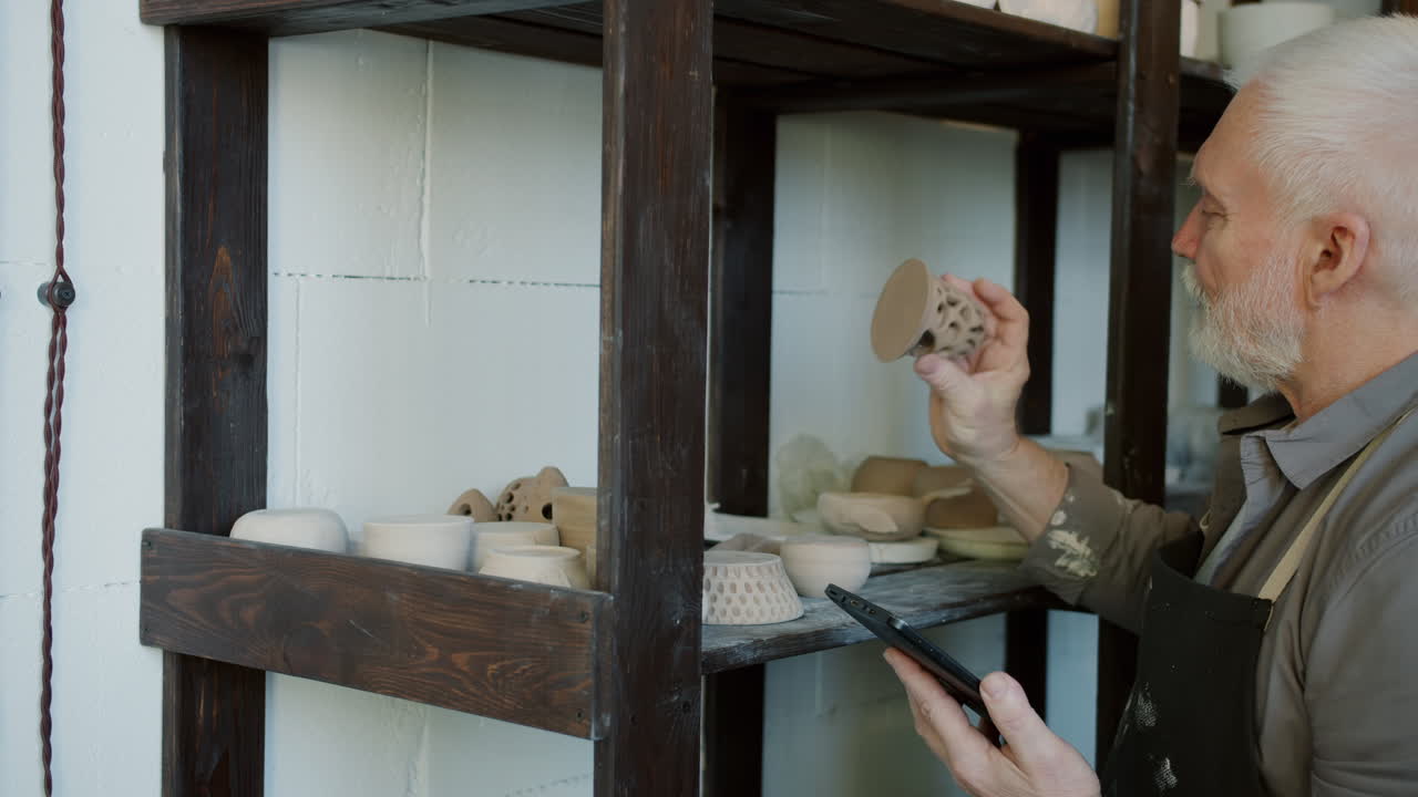 Senior Craftsman Examining Pottery Designs on Smartphone
