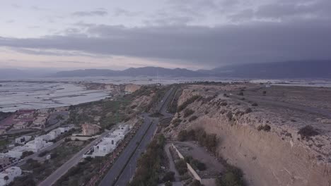 aerial view of a highway winding through a landscape with mountains, greenhouses, and a residential area