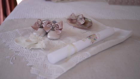 set of christening items, including a decorated candle, baby shoes with bows, and a lace seashell, arranged on a lace-covered cloth, symbolizing a sacred celebration