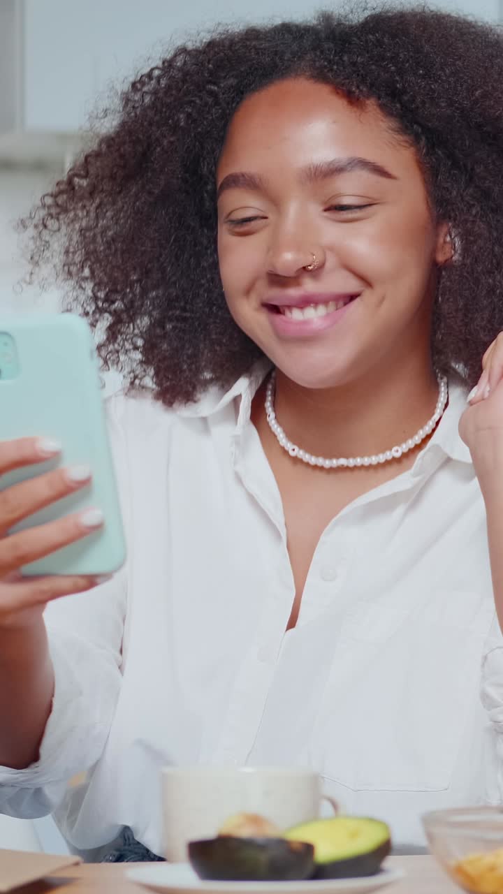 African american woman uses phone for video conferences sits at table in kitchen